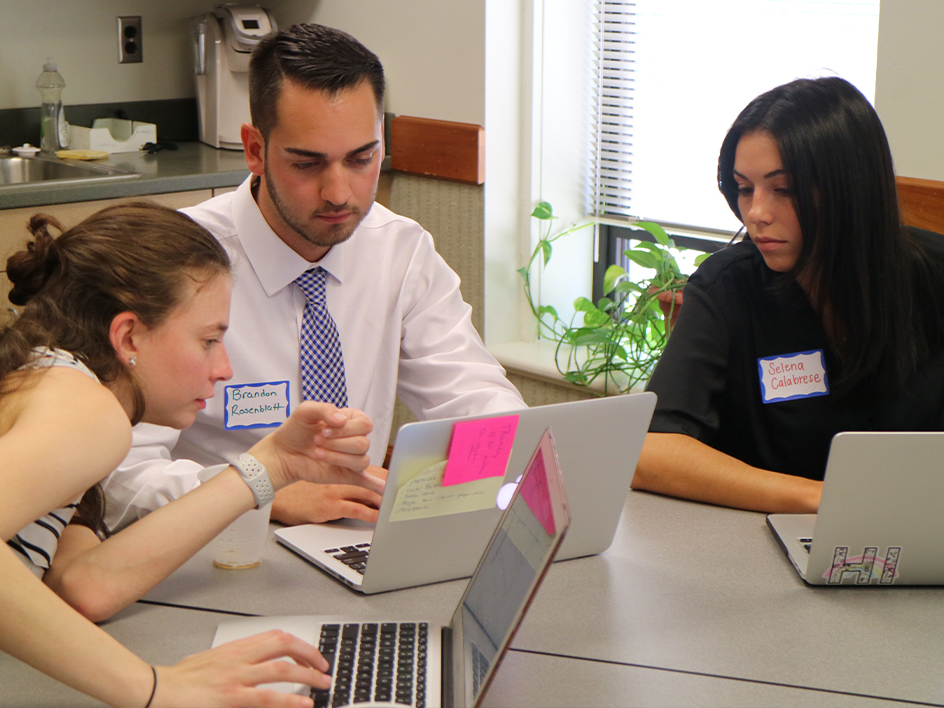 Three students collaborating on a project with their laptops