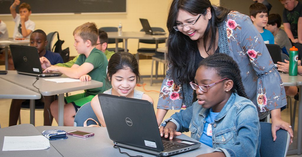 Doctoral student assists two students with an assignment on laptop