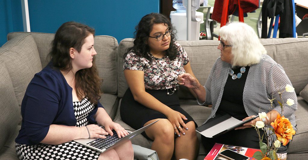 Two doctoral students speak with a professor